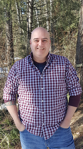 Photo of Jon, an Metis man wearing a plaid red and white shirt.